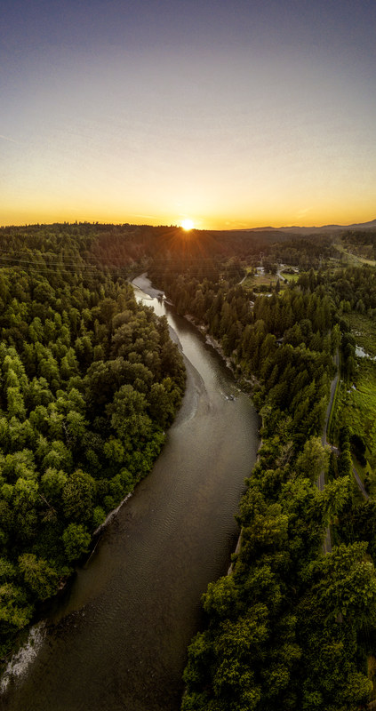 Aerial view of a winding river through dense Pacific Northwest forest at golden sunset